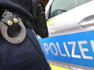 Ein Polizist mit Handschellen und einer Pistole am Gürtel steht vor einem Streifenwagen.