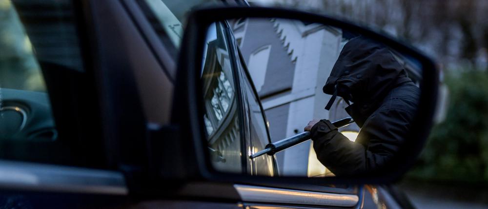 Ein Mann versucht eine Autotür mit einer Metallstange aufzubrechen (gestellte Szene). (Symbolbild)