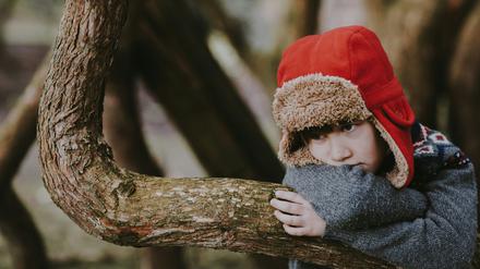 Ein kleiner Junge steht allein an einem Baum.