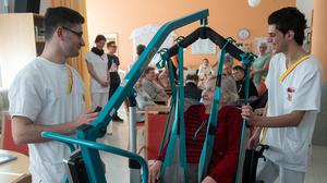 Die syrischen Flüchtlinge Ahmed Mistikalo (l.) und Bassil Alhorane helfen der Rentnerin Hildegard Hoffleuchter aus der Tagespflege am 15.2.2017 im Altenpflegeheim des Arbeiter-Samariter-Bundes (ASB) in Chemnitz (Sachsen) in den Rollstuhl.