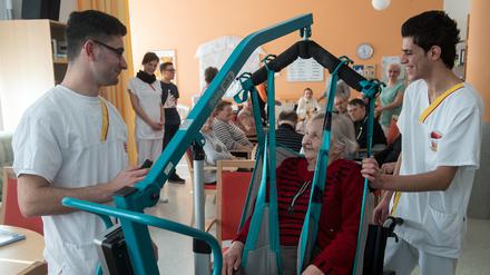 Die syrischen Flüchtlinge Ahmed Mistikalo (l.) und Bassil Alhorane helfen der Rentnerin Hildegard Hoffleuchter aus der Tagespflege am 15.2.2017 im Altenpflegeheim des Arbeiter-Samariter-Bundes (ASB) in Chemnitz (Sachsen) in den Rollstuhl.