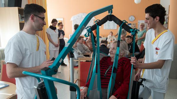 Die syrischen Flüchtlinge Ahmed Mistikalo (l.) und Bassil Alhorane helfen der Rentnerin Hildegard Hoffleuchter aus der Tagespflege am 15.2.2017 im Altenpflegeheim des Arbeiter-Samariter-Bundes (ASB) in Chemnitz (Sachsen) in den Rollstuhl.