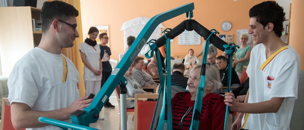 Die syrischen Flüchtlinge Ahmed Mistikalo (l.) und Bassil Alhorane helfen der Rentnerin Hildegard Hoffleuchter aus der Tagespflege am 15.2.2017 im Altenpflegeheim des Arbeiter-Samariter-Bundes (ASB) in Chemnitz (Sachsen) in den Rollstuhl.