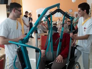 Die syrischen Flüchtlinge Ahmed Mistikalo (l) und Bassil Alhorane helfen der Rentnerin Hildegard Hoffleuchter aus der Tagespflege am 15.02.2017 im Altenpflegeheim des Arbeiter-Samariter-Bundes (ASB) in Chemnitz (Sachsen) in den Rollstuhl. Die beiden Syrer gehen mit Unterstützung des Energiedienstleisters enviaM und der Hilfs- und Wohlfahrtsorganisation ihre ersten Schritte ins Berufsleben in Deutschland. Zum 1. März werden sie als Hilfspfleger im Altenpflegeheim des ASB eingestellt. Die enviaM-Gruppe und der ASB unterstützen sich bei der Integration von Flüchtlingen. Foto: Hendrik Schmidt/dpa-Zentralbild/dpa +++(c) dpa - Bildfunk+++ | Verwendung weltweit