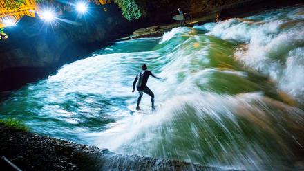 Ein Surfer reitet bei Nacht mit seinem Board über die künstliche Welle des Eisbachs im Englischen Garten (Symbolbild).