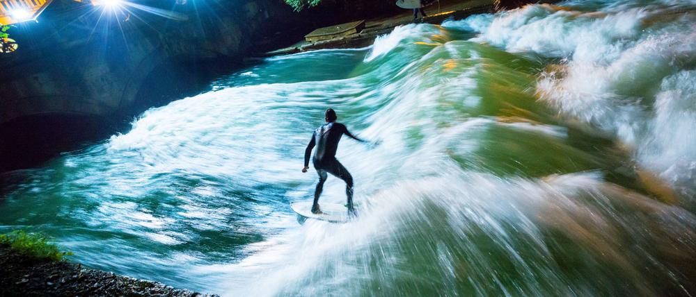 Ein Surfer reitet bei Nacht mit seinem Board über die künstliche Welle des Eisbachs im Englischen Garten (Symbolbild).