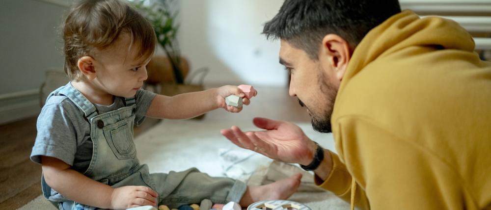 Ein Vater spielt mit seinem Sohn auf einem Teppichboden (Symbolbild)