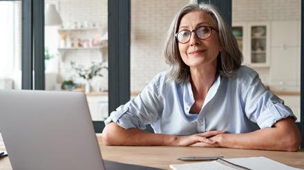 Eine Frau mit grauen Haaren sitzt vor Ihrem Laptop.