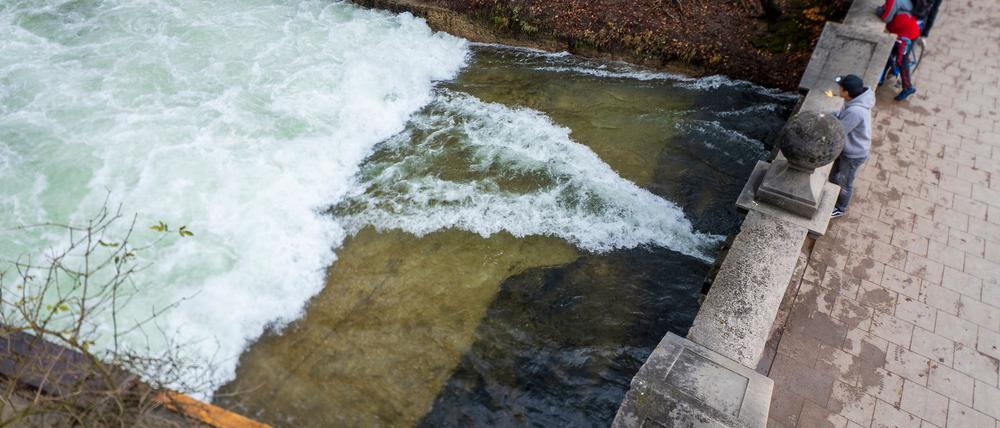 Passanten stehen an der Eisbachwelle im Englischen Garten, an der nach einer Bachreinigung nicht mehr gesurft werden kann. Die Welle ist normalerweise zu jeder Jahres- und Tageszeit ein wahrer Hotspot für Touristen und Surfer aus der ganzen Welt. 