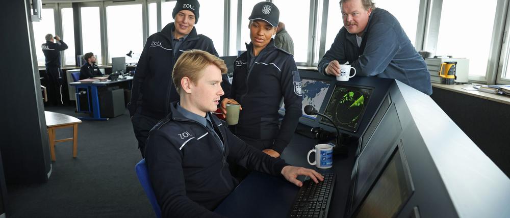 Zöllner Sven-Erik Dröse (Lukas Zumbrock, sitzend) kommt einer heißen Spur auf die Schliche in einer Szene aus der Folge „Geschäft mit dem Tod“ aus der Krimireihe „Der Bremerhaven-Krimi“ - hinten von links nach rechts: Elena Uhlig, Cynthia Micas, Bernd Hölscher.