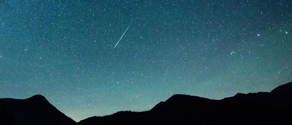 ARCHIV - 12.08.2018, Bayern, Einsiedl: Eine Sternschnuppe leuchtet neben der Milchstraße am Himmel über dem Walchensee.  (zu dpa: «Leoniden im Anflug») Foto: Matthias Balk/dpa +++ dpa-Bildfunk +++