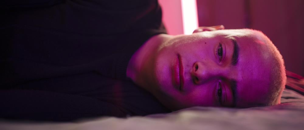 Ein traurig blickender junger Mann liegt seitlich auf einem Bett (Symbolbild).