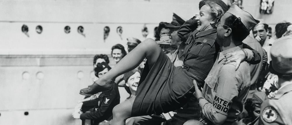 Marlene Dietrich wird von amerikanischen Soldaten auf Händen getragen.