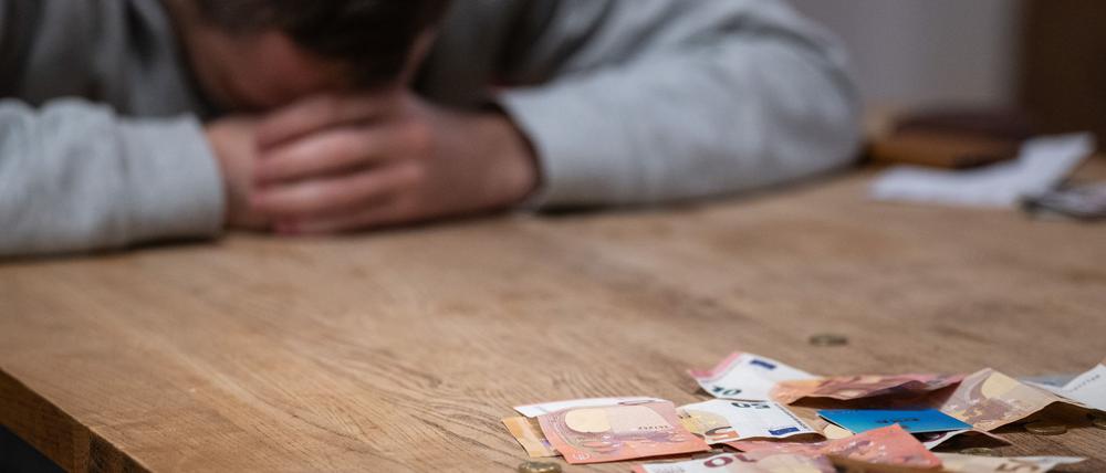 Ein Mann hat seinen Kopf auf seine Hände gelegt, während sich vor ihm Geldscheine, Münzen und Bankkarten auf einem Tisch befinden.