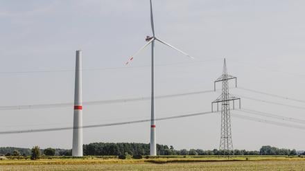 Ein Strommast steht neben einem sich im Bau befindenden Windrad sowie einem betriebenen Windrad in Waldow.