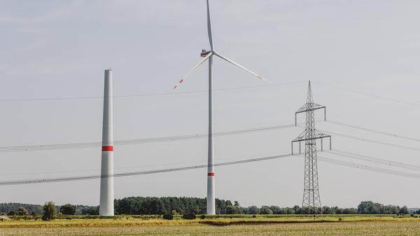 Ein Strommast steht neben einem sich im Bau befindenden Windrad sowie einem betriebenen Windrad in Waldow.