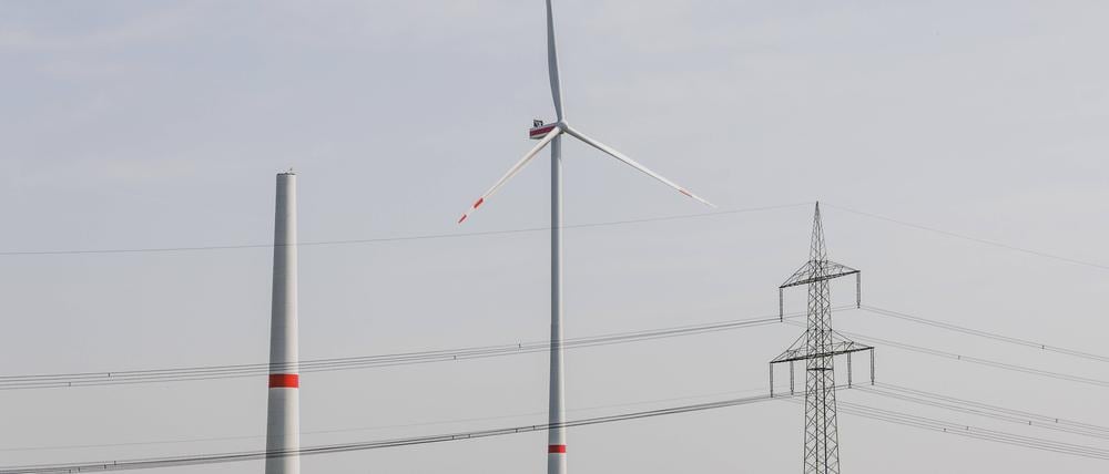 Ein Strommast steht neben einem sich im Bau befindenden Windrad sowie einem betriebenen Windrad in Waldow.
