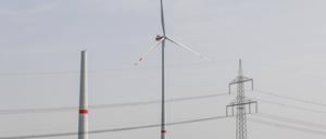 Ein Strommast steht neben einem sich im Bau befindenden Windrad sowie einem betriebenen Windrad in Waldow.