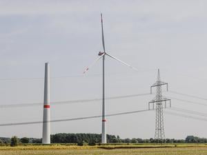 Ein Strommast steht neben einem sich im Bau befindenden Windrad sowie einem betriebenen Windrad in Waldow.