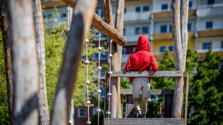 Ein Kind steht auf einem Spielplatz vor einem Plattenbau (Symbolbild).