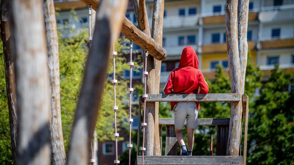 Ein Kind steht auf einem Spielplatz vor einem Plattenbau.