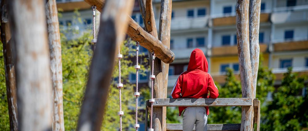 Ein Kind steht auf einem Spielplatz vor einem Plattenbau (Symbolbild).