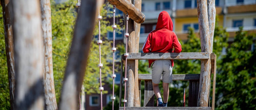 Ein Kind steht auf einem Spielplatz vor einem Plattenbau.