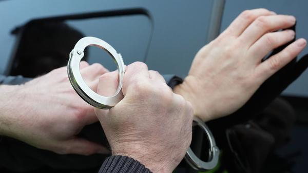 Ein Polizist legt einem Mann Handschellen an. (Symbolbild)