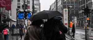 Passanten auf der Friedrichstraße teilen sich einen Regenschirm.