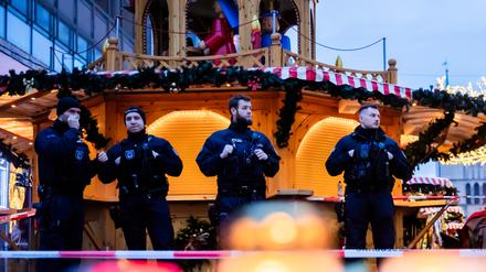 Polizisten sichern den Weihnachtsmarkt in Magdeburg, wobei Kerzen vor ihnen brennen. 