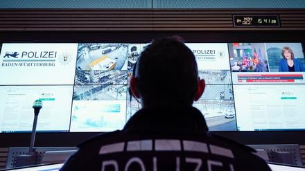 Ein Beamter steht im Führungs- und Lagezentrum des Polizeipräsidiums Mannheim vor einer Wand mit Bildschirmen.