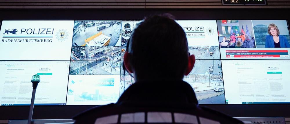 Ein Beamter steht im Führungs- und Lagezentrum des Polizeipräsidiums Mannheim vor einer Wand mit Bildschirmen.
