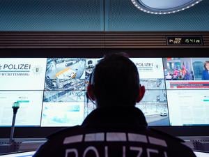 Ein Beamter steht im Führungs- und Lagezentrum des Polizeipräsidiums Mannheim vor einer Wand mit Bildschirmen.