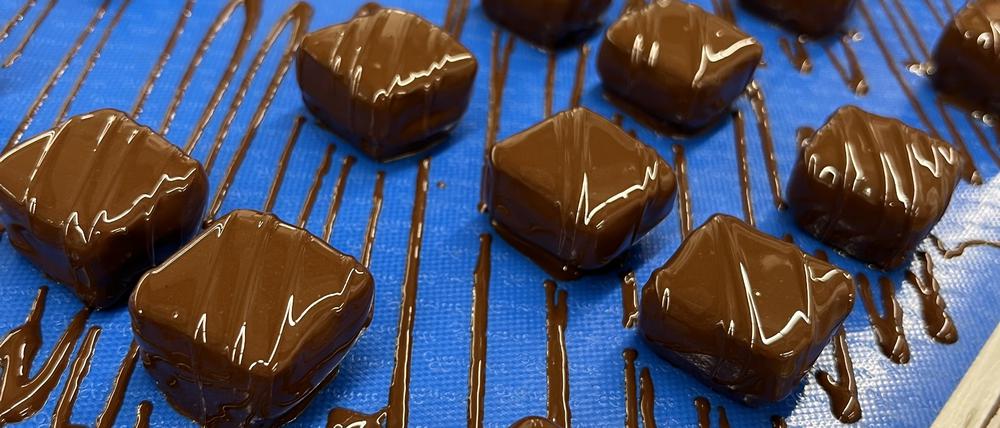 Die Sorte „Trüffel Krokant“ fährt per Laufband zur nächsten Station: Jede Praline wird fünfmal von Hand bearbeitet.