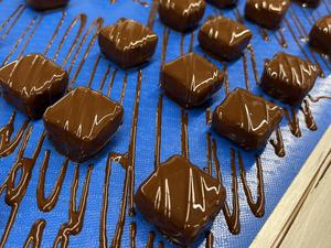 Die Sorte „Trüffel Krokant“ fährt per Laufband zur nächsten Station: Jede Praline wird fünfmal von Hand bearbeitet.