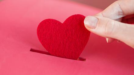 Ein rotes Herz wird in eine Spendenbox gesteckt.