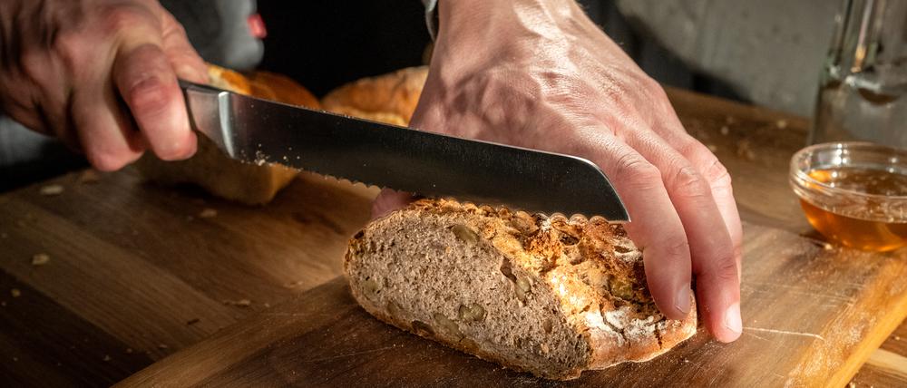 Close-up of man's hands cutting fresh loaf of bread on chopping board.