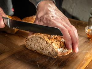 Close-up of man's hands cutting fresh loaf of bread on chopping board.