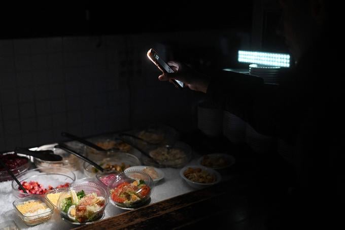 A woman uses the flashlight of her mobile phone to choose food as she visits a restaurant during a power outage in Kyiv on November 21, 2025, amid the Russian invasion of Ukraine. (Photo by Sergei GAPON / AFP)