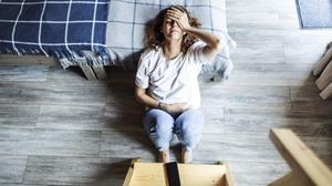 Eine junge Frau sitzt erschöpft auf dem Fußboden neben einem Bett (Symbolbild).