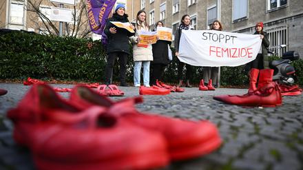 Teilnehmerinnen halten während des Hissens der Anti-Gewalt-Fahne anlässlich des Internationalen Tags für die Beseitigung von Gewalt gegen Frauen am Rathaus Tiergarten ein Banner mit der Aufschrift «Stoppt Femizide» hinter Roten Schuhen.