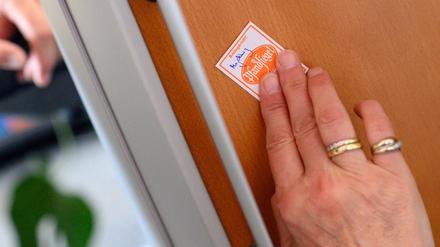 Eine Gerichtsvollzieherin klebt ein Pfandsiegel auf ein technisches Gerät. (Symbolbild)