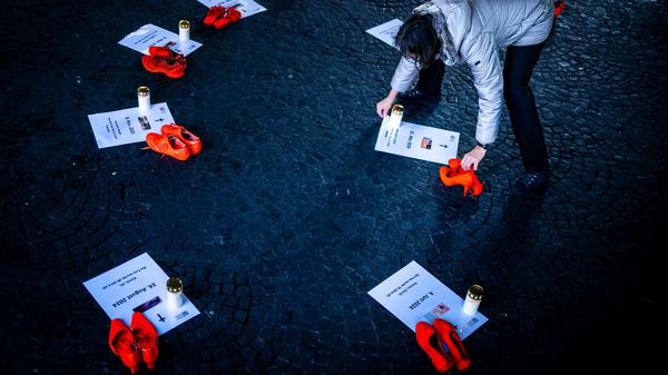 25.11.2025, Schweiz, Zürich: Eine Freiwillige platziert Kerzen neben orangen Schuhen und Plakaten für Opfer von Femiziden als Teil einer Installation "Gedenken an getoetete Frauen durch Femizide 2024 - 2025" bei der Wasserkirche, anlässlich der Kampagne 16 Tage gegen Gewalt an Frauen. Der "Internationale Tag gegen Gewalt an Frauen", auch als "Orange Day" bekannt, wird seit mehr als drei Jahrzehnten jährlich am 25. November begangen. Weltweit wird an diesem Tag mit orange beleuchteten Gebäuden, Demonstrationen und weiteren Veranstaltungen auf die anhaltende Gewalt gegen Frauen und Mädchen hingewiesen. Foto: Michael Buholzer/KEYSTONE/dpa +++ dpa-Bildfunk +++
