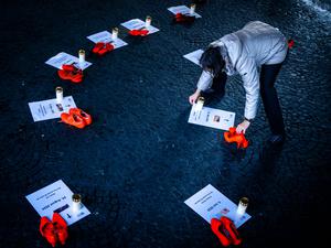25.11.2025, Schweiz, Zürich: Eine Freiwillige platziert Kerzen neben orangen Schuhen und Plakaten für Opfer von Femiziden als Teil einer Installation "Gedenken an getoetete Frauen durch Femizide 2024 - 2025" bei der Wasserkirche, anlässlich der Kampagne 16 Tage gegen Gewalt an Frauen. Der "Internationale Tag gegen Gewalt an Frauen", auch als "Orange Day" bekannt, wird seit mehr als drei Jahrzehnten jährlich am 25. November begangen. Weltweit wird an diesem Tag mit orange beleuchteten Gebäuden, Demonstrationen und weiteren Veranstaltungen auf die anhaltende Gewalt gegen Frauen und Mädchen hingewiesen. Foto: Michael Buholzer/KEYSTONE/dpa +++ dpa-Bildfunk +++