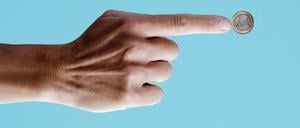 Der Zeigefinger einer männlichen Hand zeigt auf eine Ein-Euro-Münze.