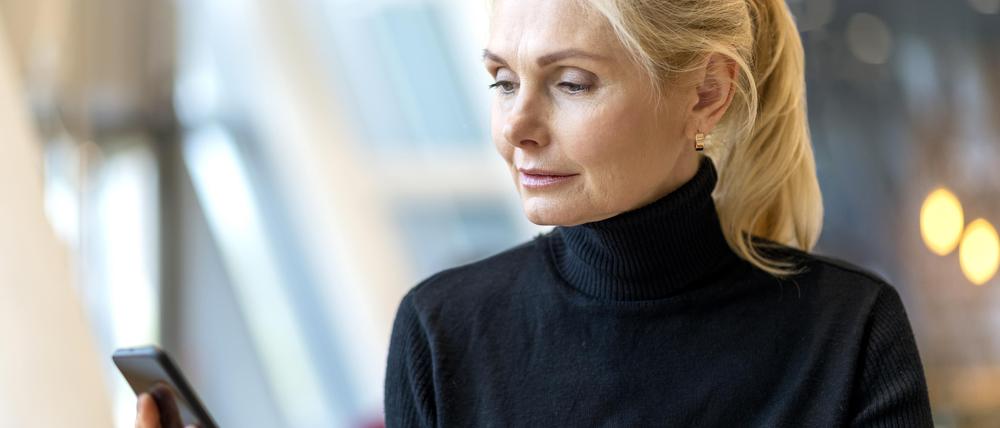 Eine Frau blickt prüfend auf ihr Smartphone.  