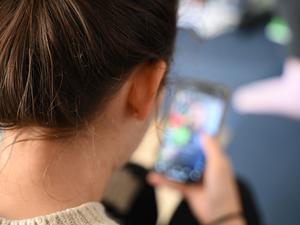 Symbolbild: Eine Person öffnet auf ihrem Smartphone einen Ordner mit Apps verschiedener sozialer Medien. 