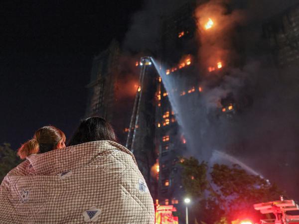 Residents wrapped in blankets watch flames engulf bamboo scaffolding at Wang Fuk Court housing estate after a major fire broke out, in Tai Po, Hong Kong, China, November 26, 2025. REUTERS/Tyrone Siu     TPX IMAGES OF THE DAY     