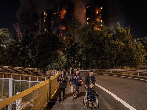 People leave the scene of a major fire that engulfed several apartment blocks at the Wang Fuk Court residential estate in Hong Kong's Tai Po district on November 26, 2025. A huge fire ripped through several high-rise blocks in a Hong Kong residential estate on November 26, killing at least 13 people, with media reporting that some residents were trapped inside. (Photo by AFP)