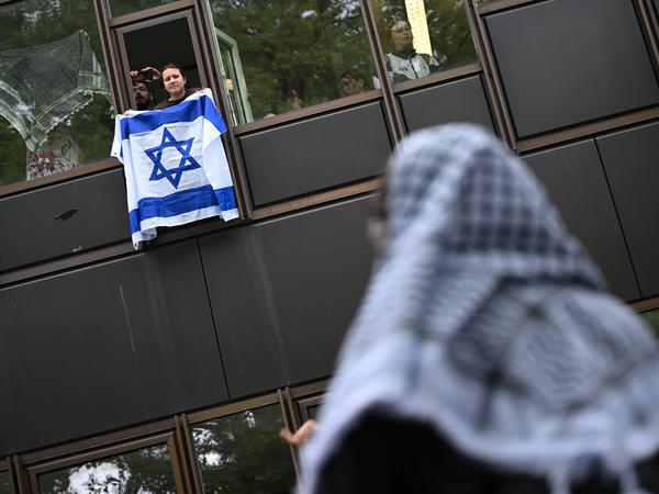 Eine Frau hält während einer propalästinensischen Demonstration der Gruppe «Student Coalition Berlin» auf dem Theaterhof der Freien Universität Berlin vor Unterstützern außerhalb des Camps eine Israelflagge aus einem Fenster. Die Teilnehmer haben am Dienstagvormittag den Platz mit Zelten besetzt. +++ dpa-Bildfunk +++